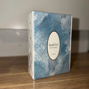 Victoria parfym från Lattafa - Säljer en Victoria parfym från Lattafa i en snygg blå och vit förpackning med silverdetaljer och ett elegant mönster. Boxen har en oval etikett framtill med både arabisk och engelsk text. Perfekt för dig som gillar exklusiva dofter.