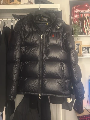 Svart puffer dunjacka med dragkedja - Snygg svart dunjacka i puffer-modell med glansig finish och dragkedja framtill. Jackan har lång ärm och en klassisk, lite oversized passform som passar perfekt till kalla dagar. Har kvitto inga skador helt ny använd fåtal gånger, säljs för den då är för stor. Hör av er vid intresse