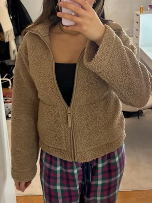 Beige teddyjacka med dragkedja - Mysig beige teddyjacka med hel dragkedja framtill och hög krage. Jackan har en loose passform och är tillverkad i fluffigt teddy-material som håller dig varm. Perfekt för kyliga dagar och enkel att matcha med olika outfits.