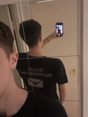 Svart bvaldi Valentines Day t-shirt - Svart t-shirt från bvaldi med texten 'VALENTINES DAY' och ett kuvert med hjärta på ryggen. T-shirten har korta ärmar och normal passform. Perfekt för dig som vill sticka ut med en unik och snygg detalj på ryggen.