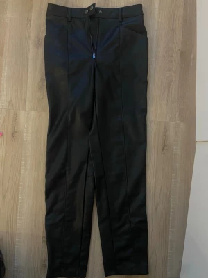 Svarta skinnbyxor med dragkedja - Snygga svarta skinnbyxor med raka ben och dragkedja fram. Byxorna har bälteshällor och diskreta sömdetaljer längs benen. Endast använda 1 gång då de är lite för stora. mycket bra skick. Nypris: 150kr. 