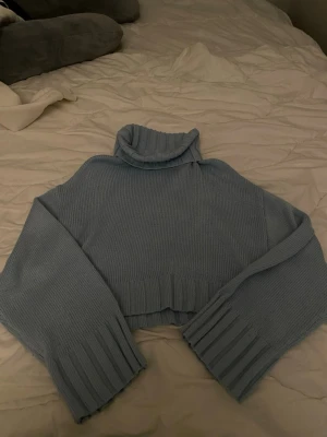 Ljusblå polotröja från Divided - Säljer en ljusblå stickad polotröja från H&M. Tröjan har breda ribbade muddar vid ärmslut och nederkant samt en hög, mysig polokrage. Perfekt för dig som gillar oversized ärmar och en chill vibe. 