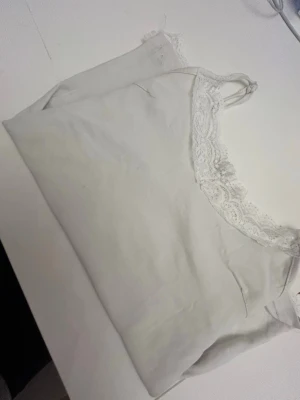 Vitt nattlinne med spetsdetaljer - Sött vitt nattlinne med tunna axelband och fina spetsdetaljer längs urringning och nederkant. Mjukt och lätt material som känns skönt mot huden. Perfekt för mysiga kvällar hemma.