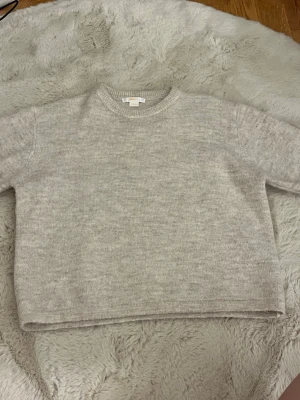 Beige stickad tröja från Gina Tricot - Mysig beige stickad tröja från Gina Tricot med rund halsringning och ribbade muddar vid ärmslut och nederkant. Perfekt för lager på lager och enkel att matcha med olika outfits. Tillverkad i mjukt material för extra komfort.