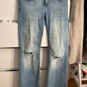 Bootcut jeans med slitningar från Nelly - Bootcut jeans i ljusblå tvätt från Nelly, låg midja och slitna detaljer vid knäna. Lite slitna nertill på vänster ben 