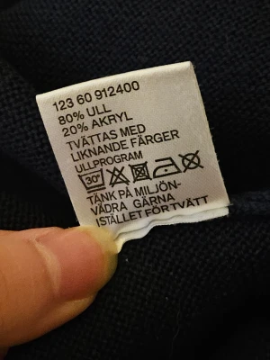 Mörkblå stickad tröja från Wera - Mörkblå stickad tröja från Wera med rund hals och lång ärm. Tröjan har en rak passform och är tillverkad i 80% ull och 20% akryl, vilket gör den både mjuk och varm. Perfekt för dig som gillar enkel och stilren design.