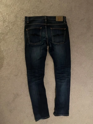 Nudie jeans - Skit feta nudie jeans i mörkblå. Jeansen har riktigt snygg färg och passform. De har ett litet hål men jag tycker det bara gör jeansen snyggare. De har storleken W32 L32. Skriv vid funderingar! 