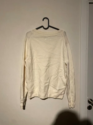 V-ringad beige stickad tröja Weekday - Säljer en beige stickad tröja från Weekday med snygg v-ringning och ribbade muddar vid ärmslut och nederkant. Tröjan har lång ärm och en relaxed passform som är perfekt för chill dagar. Enkel och stilren design som funkar till allt.