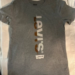 Grå Levi's t-shirt - Snygg grå t-shirt från Levi's med vertikalt logotryck i vitt och gula på framsidan. Klassisk rund hals och korta ärmar. 