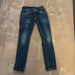 Dondup jeans - Snygga dondup jeans i mörkblå tvätt med slitningar och distressed detaljer på benen. Klassisk femficksmodell med raka ben och kontrastsömmar. Perfekt för dig som gillar en cool och avslappnad stil.