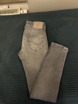 Grå skinny jeans från Jack & Jones - Snygga grå jeans från Jack & Jones med klassisk femficksdesign och ljus tvätt. Jeansen har raka ben och normal passform, med stilrena sömmar och en diskret logotyp på bakfickan. Perfekt för dig som gillar en clean och modern look.