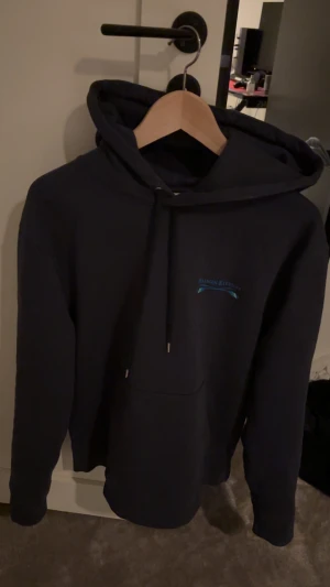 Mörkblå hoodie Maison Kitsuné M - Snygg mörkblå hoodie från Maison Kitsuné i storlek M. Tröjan har huva med snörning, en stor magficka och diskret logga i blått på bröstet. Perfekt för dig som gillar stilrena och bekväma plagg med streetkänsla. Orderbekräftelse finns och är köpt från ricodeluxery och den är använd 1 gång så i super skick