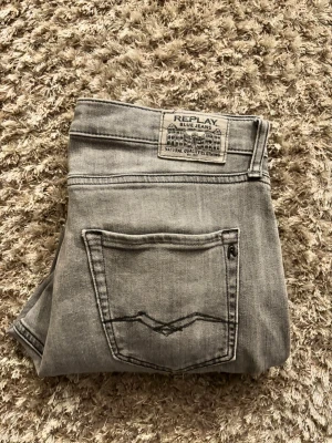 Replay Thad grå jeans straight fit - Snygga grå jeans från Replay, modell Thad. Klassisk femficksdesign med raka ben och svarta detaljer på knapp och ficka. Jeansen har en neutral grå tvätt och är tillverkade i slitstarkt denimtyg. Perfekt för dig som gillar stilrena och tidlösa jeans. Jensens storleks lapp har blivit bortklippt från den förra ägaren men jag har storlek 32/32 och jag skulle säga att de sitter som 32/33 eller 32/34. Det är även lite större nertill men det är inget problem. Har du fler frågor så är det bara att fråga