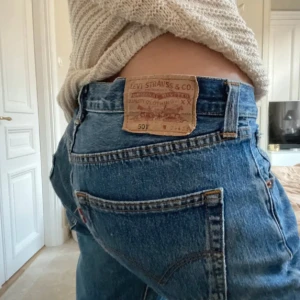 Levi's 501 blå jeans med hål på knät - Säljer ett par klassiska eftertraktade Levi's 501 jeans i blå denim. Modellen är utsvängd i passformen och låg midja med ett snyggt hål på ena knät. Ikonisk läderpatch baktill. Det är ett par perfekta och tidlösa jeans. 