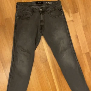 Grå Replay Anbass - Storlek: 31/32. Snygga Replay Anbass jeans i mörkgrå tvätt med den klassiska framficksdesignen. Modellen har smal passform och är tillverkad i stretchigt jeanstyg för skön komfort. Perfekt för dig som gillar stilrena och moderna jeans.