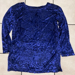 Blå sammet topp med zebramönster storlek M/L - Snygg blå topp i sammet med lång ärm och coolt zebramönster. Materialet är mjukt och har en glansig finish som ger extra attityd. Perfekt för dig som gillar att sticka ut med unika detaljer.