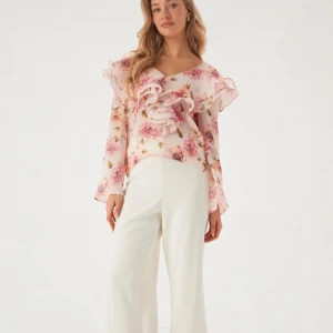Blommig volangblus från Bubbleroom -  Blusen har volangdetaljer framtill och på ärmarna, v-ringning och öppen rygg med knytband. Långärmad och i ett lätt, transparent material som känns luftigt och vårigt.
