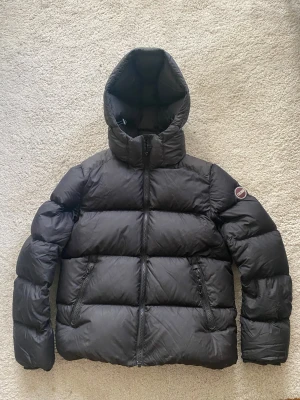 Svart Colmar pufferjacka med huva - Svart pufferjacka från Colmar i storlek y12/ 154cm, men passar mig som har storlek xs. Säljer då jag har andra jackor jag använder mer. Pris kan diskuteras! 