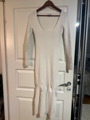 Vit ribbad långklänning från Ganni - Långklänning från Ganni i ribbad, vit stickat tyg. Klänningen har lång ärm men en liten skurning i armslutet, djup rundad halsringning och en figurnära passform. Storlek M, endast använd vid ett tillfälle.