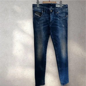 Blå skinny jeans från Diesel - Snygga blå jeans från Diesel med slitna detaljer och klassisk femficksdesign. Modellen är skinny med smal passform och stretchigt material för extra komfort. Jeansens tvättade look ger en cool vibe och de har normal midja med knapp och dragkedja framtill. #diesel #jeans
