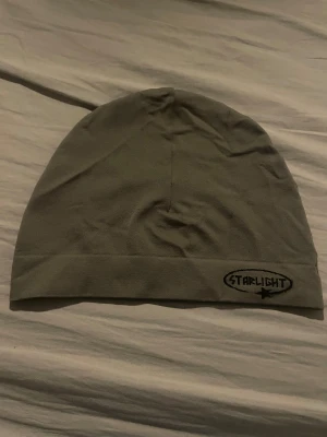 Grå mössa från Starlight - Enkel och stilren grå mössa från Starlight med svart broderad logga framtill. Mössan har en klassisk, rundad form och är tillverkad i mjuk bomull som känns skön mot huden. Perfekt accessoar för kyligare dagar.