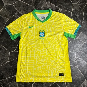 Brasilien Nike fotbollströja - Säljer en Brasilien fotbollströja från Nike i gul med gröna detaljer och blå mönster på ärmsluten. Tröjan har korta ärmar, V-ringad krage och är tillverkad i lätt polyester. Framsidan har Brasilien-emblem och ett abstrakt vitt mönster över hela tyget.
