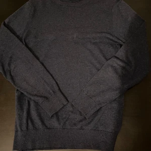 Mörkblå stickad tröja - En enkel och stilren mörkblå stickad tröja med rund hals och långa ärmar. Tröjan har ribbade muddar vid ärmslut och nederkant, vilket ger en schysst passform. Perfekt för dig som gillar klassiska och tidlösa plagg.