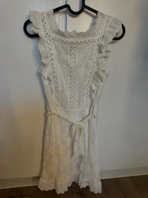 Vit spetsklänning från Dennis Maglic - Superfin vit klänning från Dennis Maglic i Strl S. Klänningen har superfina spetsdetaljer, volanger längs axlarna och ett knytband i midjan. Perfekt för sommaren och studenten🤗🌸
