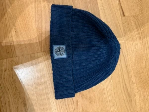 Stickad mössa Stone Island - Stickad marinblå mössa från Stone island. Använd men i fint skick!