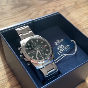 Festina Chronograph grön/silver herrklocka - Snygg Festina Chronograph herrklocka med grön urtavla och silverfärgat armband i metall. Klockan har flera subdials, datumvisning och markerade index. Robust design med sportig känsla och klassisk rund form. Perfekt för dig som gillar stilrena accessoarer.