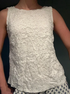 Vit blommig spetslinnetopp från Stockh lm - Säljer en vit linnetopp från Stockh lm med blommigt spetsmönster. Toppen är ärmlös och har rund halsringning. Materialet är mjukt och har ett innerfoder som gör den bekväm att bära. Perfekt för dig som gillar romantiska detaljer och fräsch stil.