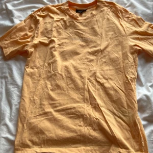 Beige/orange t-shirt  - Snygg beige t-shirt från Icono Couture med tryck 'ICONO COUTURE PARIS / TOKYO' på bröstet. Modellen är relaxed fit med rund hals och korta ärmar. Perfekt för dig som gillar stilrena och enkla plagg med en modern touch.