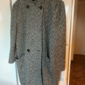 Rutig ullkappa från H&M Citylook - Snygg rutig kappa från H&M Citylook i svart och vit. Klassisk rak modell med dubbelknäppning och fickor fram. Materialmix med 40% ull, 25% polyester och 20% akryl, fodrad med nylon. Perfekt för dig som gillar tidlös stil och vill ha en jacka som sticker ut.