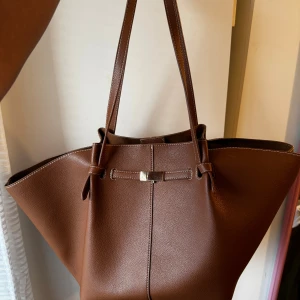 Brun axelväska i skinn med gulddetalj - Snygg brun axelväska i skinn med stilren design och guldfärgad metallspänne framtill. Gott som ny 