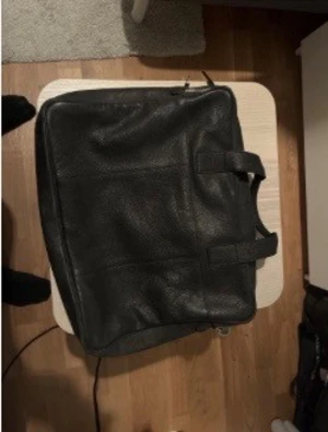Svart tiger of sweden portfölj i skinn med dragkedja - Stilren svart portfölj i äkta skinn med praktiskt handtag och en snygg dragkedjedetalj på framsidan. Perfekt för att bära laptop, papper och andra viktiga grejer till skolan eller jobbet. Enkel och klassisk design som passar till allt. Ny pris 3000kr.