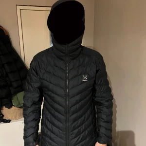 Svart dunjacka från Haglöfs, M - Säljer en svart dunjacka från Haglöfs i storlek M. Jackan har huva, dragkedja hela vägen och quiltad design. Perfekt för kalla dagar och riktigt skön att bära. Klassisk look med diskret Haglöfs-logga på bröstet. 