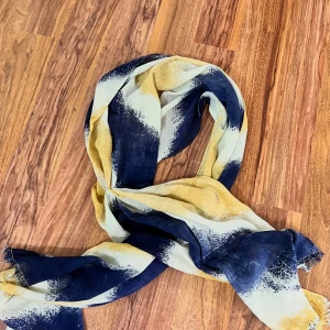 Randig halsduk i blått och gult - Snygg halsduk med breda, randiga fält i marinblått, gult och vitt. Mjukt och lätt material som gör den enkel att styla runt halsen eller över axlarna. Perfekt accessoar för att lyfta din outfit med lite färg och mönster.