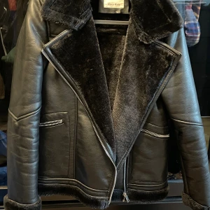 Svart pälsfodrad jacka från Zara Kids - Snygg svart jacka från Zara Kids med mjukt pälsfoder och bred krage. Jackan har dragkedjor på fickorna och framtill, samt detaljer i skinnimitation. Perfekt för kalla dagar med sin varma insida och coola look.