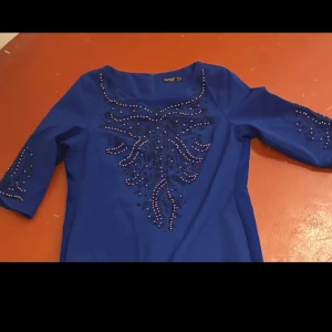 Blå klänning med pärldetaljer - Snygg blå klänning från Panky med halvärmar och dekorativa pärlor framtill och på ärmarna. Klänningen har en rak passform och rundad halsringning. Perfekt för dig som gillar att sticka ut med coola detaljer och färg.