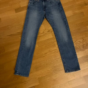 Levi's 502 blå jeans straight fit - Säljer ett par Levi's 502 Premium jeans i klassisk blå tvätt. Jeansen har rak passform, fem fickor och snygga slitningar på låren. Ikonisk röd Levi's-tag på bakfickan och läderpatch i midjan. Perfekta för en avslappnad och stilren look.