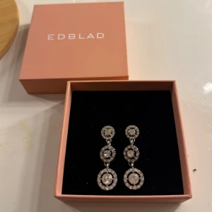 Glittriga örhängen  - Säljer ett par eleganta hängande örhängen i silverfärg med tre runda länkar på varje örhänge, dekorerade med gnistrande stenar. Perfekta för att lyfta din stil med extra bling och glam.