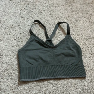 Mörkgrön ribbad gymtopp - Snygg mörkgrå linnetopp med ribbad kant och smala axelband som korsas i ryggen. Skön att gymma med.