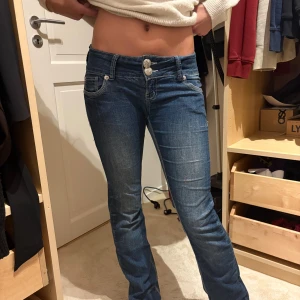 Blå lågmidjade bootcut jeans - Snygga blå jeans med låg midja och bootcut passform. Jeansen har två dekorativa knappar framtill, klassiska fickor och coola sömmar på bakfickorna. Materialet är jeans med lätt slitning för en trendig look. Storlek xs/s dom är väldigt stretchiga 