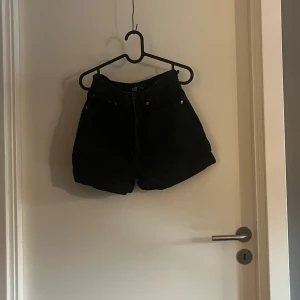 Svarta denimshorts från lager 157 - Svarta denimshorts från lager 157 med klassisk femficksdesign och uppvikta benslut. Modellen är högmidjad och har knapp och dragkedja framtill. Storlek S.