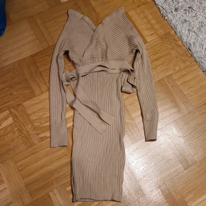 Beige ribbad omlottklänning Shein - Ribbad beige omlottklänning från Shein med lång ärm och knytband i midjan. Klänningen är figurnära och har v-ringad omlottfront som ger en snygg siluett. Perfekt för dig som gillar stilrena och trendiga plagg.