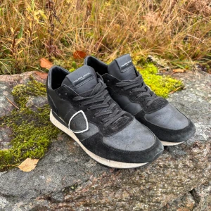 Philippe model skor - Svarta sneakers från Philippe Model med snygga detaljer i mocka och skinn. Klassisk rund tå, snörning och vit sula med svart rand. Märkets logga på sidan och hälen. Perfekt för dig som gillar stilrena och sportiga skor.
