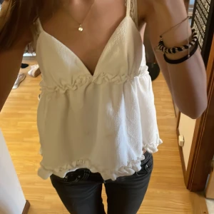 Vit linnetopp med volang från SHEIN - Supersöt vit linnetopp från SHEIN med smala axelband och v-ringad front. Toppen har volangdetaljer både vid midjan och nederkanten som ger en extra girly vibe. Materialet är lätt och skönt, tillverkat av polyester med lite stretch för en bekväm passform.