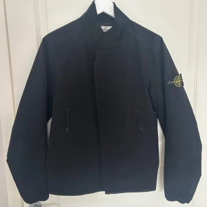 Svart jacka från Stone Island - Svart jacka från Stone Island med klassisk patch på vänster ärm. Jackan är i storlek S och den är i ett fantastiskt skick, då den knappt är använd. Nypris är 5000kr. Är det något ni undrar över eller vill ha mer bilder är det bara att höra av dig!