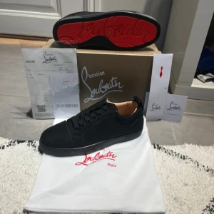 Christian Louboutin svarta sneakers - Snygga svarta sneakers från Christian Louboutin med klassisk röd sula och ovandel i mocka. Skorna har rund tå, snörning och diskret branding på insidan. Perfekta för dig som gillar lyxiga detaljer och stilren design.