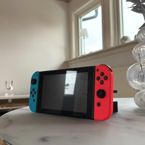 Nintendo Switch - Nintendo Switch med blå och röd Joy-Con, dockningsstation, handkontrollhållare, laddare och originalväska. Konsolen och tillbehören ser ut att vara i mycket gott skick utan synligt slitage. Perfekt för både bärbart och stationärt spelande. Pris kan diskuteras ! 